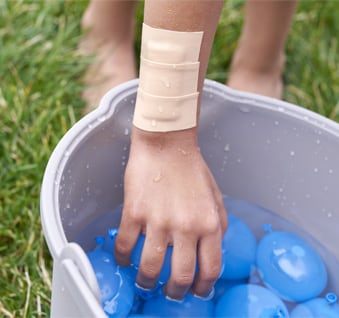 Mano con apósito colocado con cinta impermeable tomando un globo.